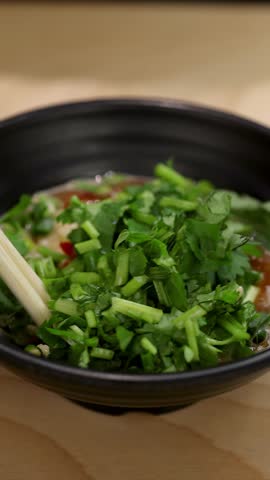Close-up of chopsticks mixing vibrant Asian chili garlic dipping sauce with fresh herbs