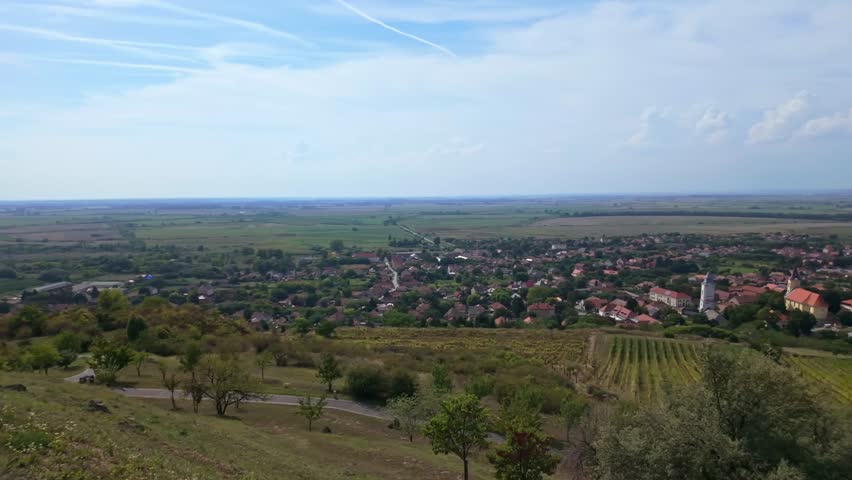 A panoramic view of Tarcal, Hungary, as the camera pans right, revealing the village, Tokaj-hegyalja vineyards, rolling fields, and a tranquil countryside under a clear autumn sky.