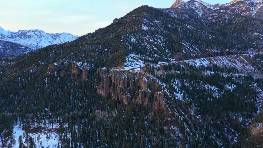 Aerial view of Highway 160 winding through the rugged San Juan Mountains at Wolf Creek Pass. The road is carved into the steep, snowy cliffs, showcasing the dramatic scale of the winter landscape.