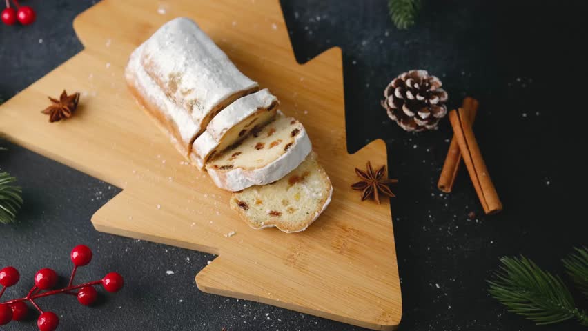 Classic Christmas Stollen dusted with powdered sugar on a wooden tree board with cinnamon sticks and pine cone.