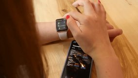 Woman using a smartwatch synced with an iPhone on a table, illustrating wearable technology, digital connectivity, and modern smart devices in everyday life. - Powered by Shutterstock - Get 15% off with code: PIKWIZARD15