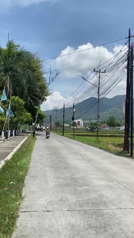 Scenic village road beneath a majestic mountain in rural Indonesia, surrounded by trees and peaceful countryside atmosphere