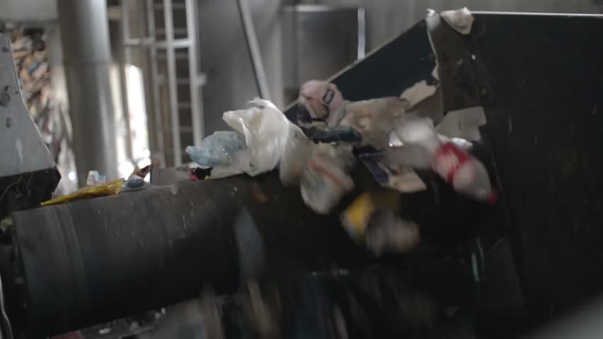 Plastic trash moves on a conveyor belt at a garbage sorting station, illustrating waste management, recycling processes, and environmental sustainability efforts.