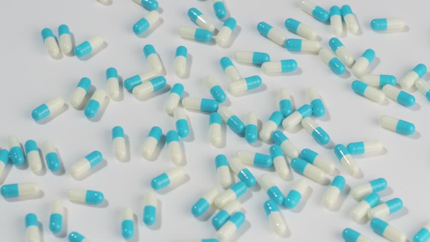 Blue and white medical capsules rotate on white surface, showing pharmaceutical dosage concept for healthcare and pharmacy.