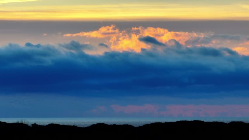 Aerial drone timelapse sliding along vibrant sunset clouds. Dramatic hyperlapse movement following colorful red and orange cloud formations across the evening sky
