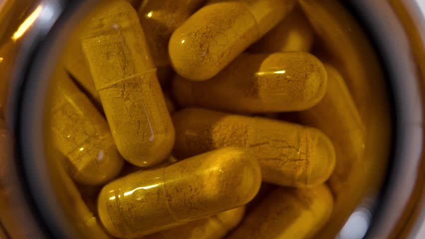 Top view of turmeric supplement capsules slowly rotating inside amber bottle, clean macro background for health product ads.