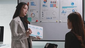 Two asian female colleagues discussing business strategy using data visualizations on a whiteboard - Powered by Shutterstock - Get 15% off with code: PIKWIZARD15