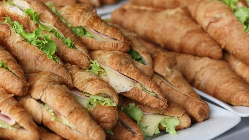 Close up of a pile of fresh croissants filled with ham, cheese, and green leaves showing baked pastry, delicious snack, breakfast concept, and food presentation for culinary ideas