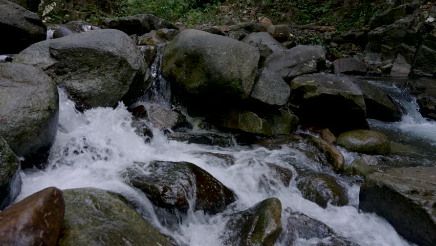 Whitewater rushing rapidly over brown and gray boulders in forest stream inside national park in Chanthaburi Thailand showing energetic water flow and natural stone texture