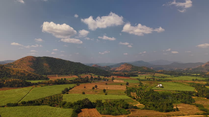 Aerial drone view rural farmland Thailand mountain valley landscape green fields patchwork trees small houses peaceful atmosphere warm sunlight scenic destination natural countryside travel