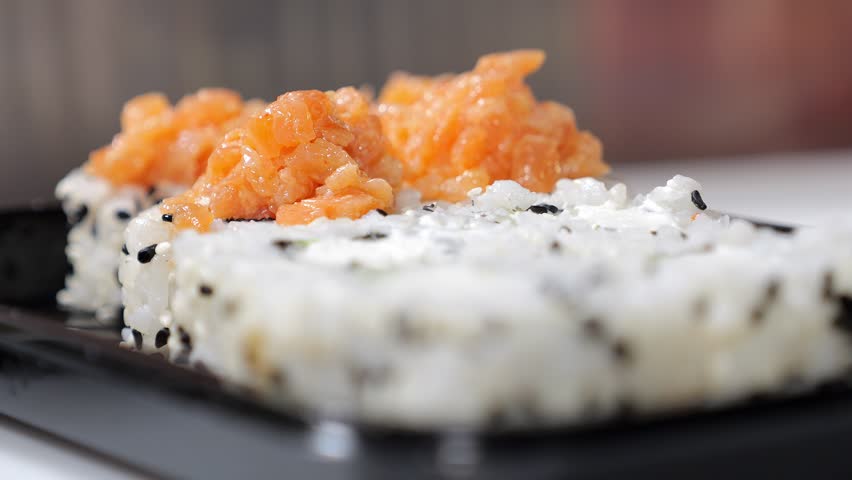 Close-up of a chef wearing gloves putting sliced salmon on sushi before baking, cooking baked sushi in the kitchen of a Japanese restaurant.