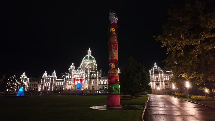Gimbal wide panning shot of a First Nations totem pole at the Parliament Buildings on a rainy night in Victoria, British Columbia, Canada. 4K
