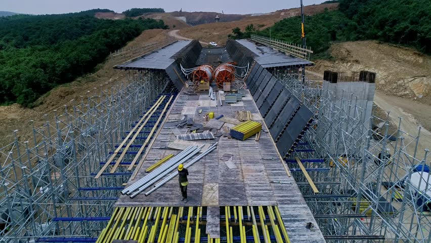 Drone view of a large viaduct deck under construction with extensive scaffolding and formwork at a highway construction site. Civil engineering and infrastructure development in mountainous terrain.