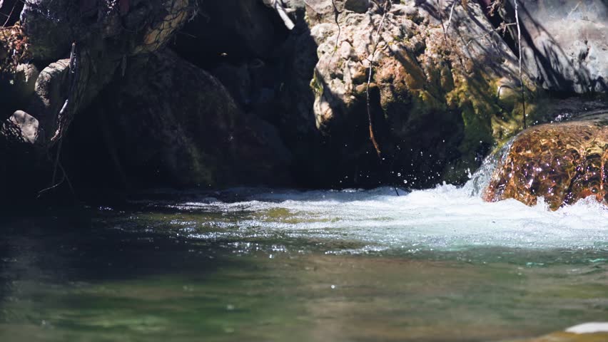 Low-angle shot of a cold, high-altitude river (Aragon River) with sunlight catching the spray and movement of the rushing water against the dark, textured rocks
