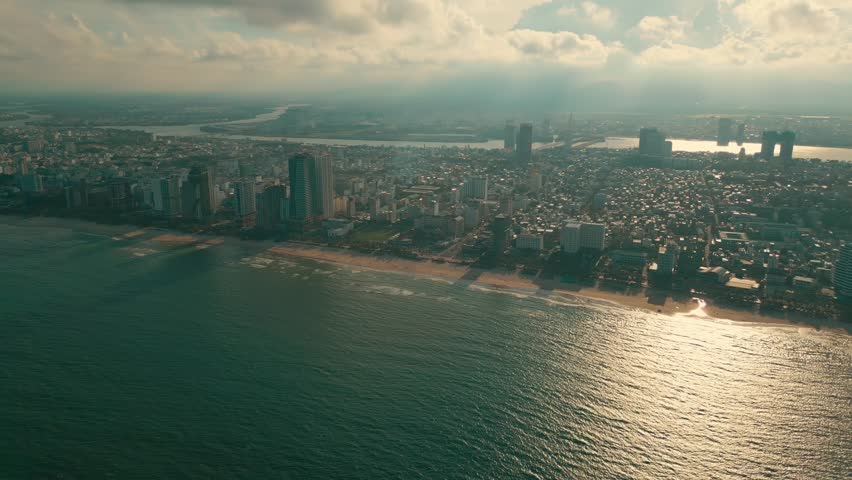 sunny sunset in Vietnamese coastal Da Nang city, My Khe sand beach and touristic My An and Son Tra district with modern skyscraper hotels and resorts, blue sea of Danang, Vietnam, aerial drone view 4k