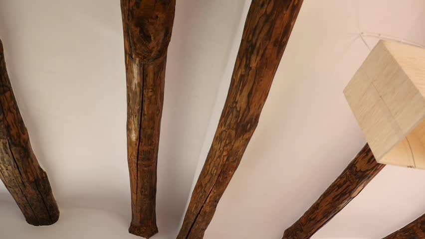 Interior ceiling with rustic chestnut wood beams against a white background and a modern minimalist design lamp. Traditional and contemporary interior architecture.
