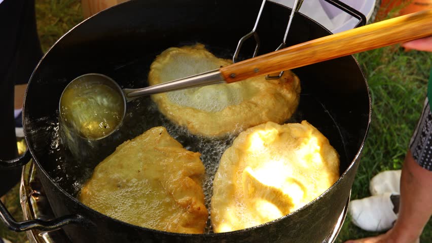 Traditionally way of cooking, frying dough in oil or pork fats making delicious treat in a large rustic pot, deep iron cauldron over open fire.