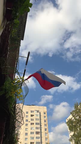 The Russian white, blue, red flag flutters against the backdrop of a building on a sunny summer day
