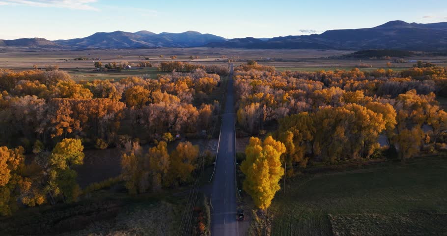 Aerial drone shot tracking low over a road and bridge crossing the Animas River, Colorado, surrounded by vibrant autumn foliage, with warm sunset light casting a peaceful glow over the fall landscape.