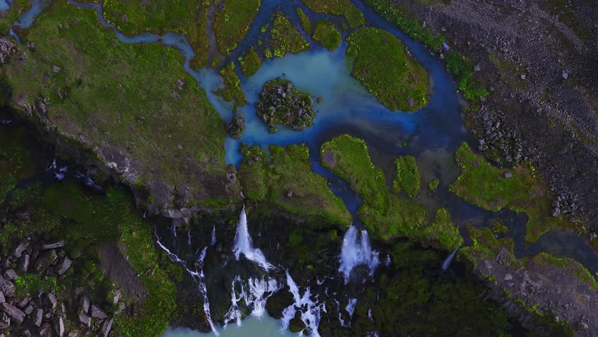 Beautiful Sigoldugljufur Canyon features a turquoise river, rugged cliffs, green moss, a serene lake, and distant mountains under a partly cloudy sky.