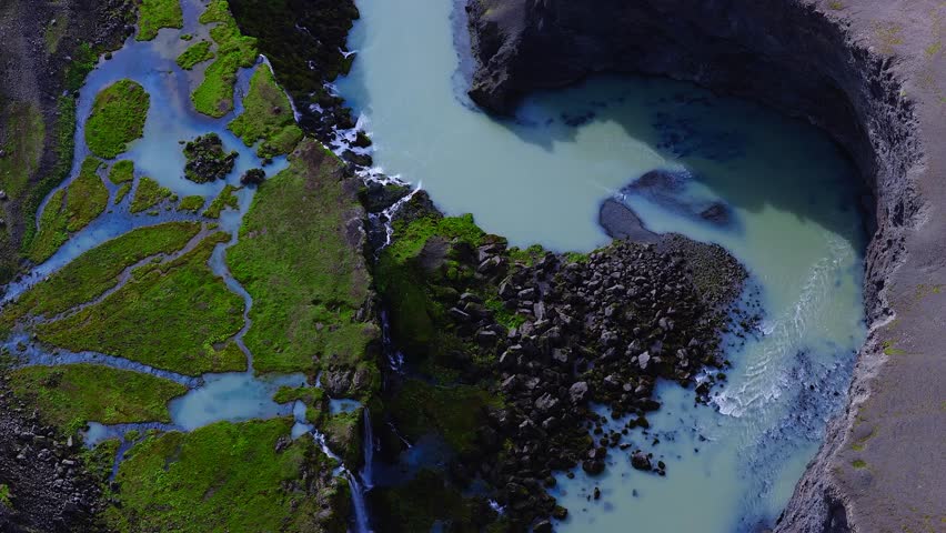 Beautiful Sigoldugljufur Canyon features a turquoise river, rugged cliffs, green moss, a serene lake, and distant mountains under a partly cloudy sky.