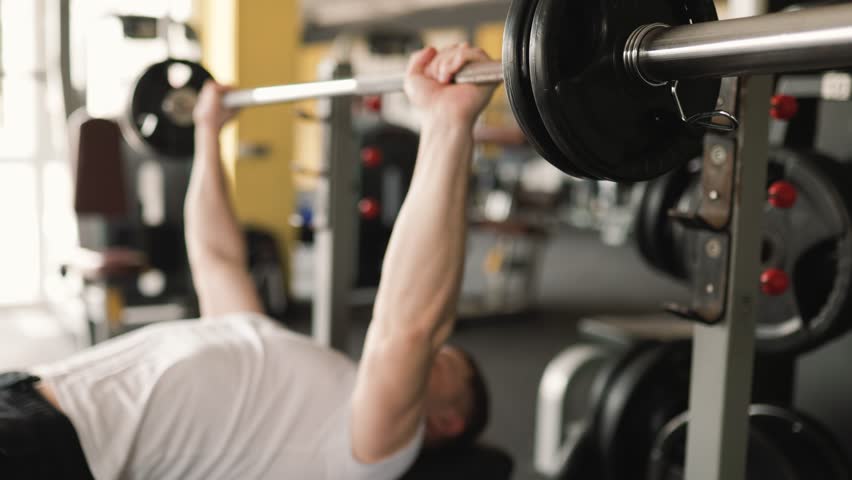A focused man in sportswear, executing a challenging barbell workout as part of his rigorous training regimen in the gym. Active Lifestyle Man Engaging in Gym Training with Barbell