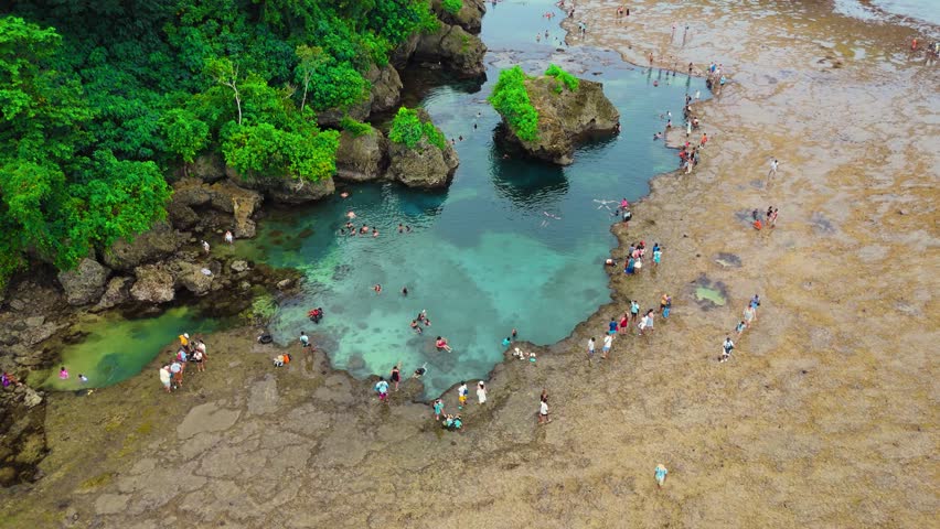 People swimming and walking around tidal pools and rugged rock formations captured with an aerial drone, Magpupungko, Siargao Island, Philippines.