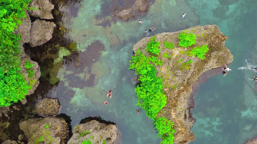 Aerial drone view of the Magpupungko tidal pools and exposed reef flats with many people swimming and exploring the coastal rock formations in Siargao, Philippines.