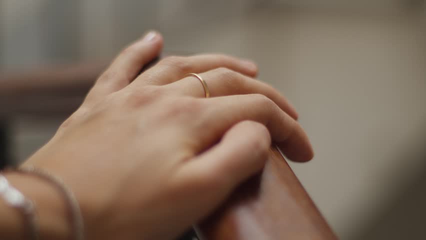 Close-up of a hand with a gold ring gently sliding down a smooth wooden railing.