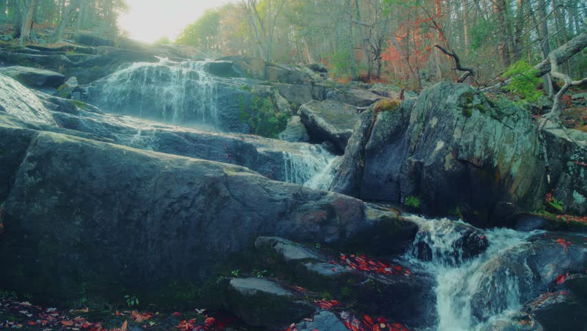 Scenic view of the Glendale Falls waterfall in Middlefield, Massachusetts, as water flows over dark, mossy rocks amidst a forest setting. The footage captures the natural beauty and tranquil movement
