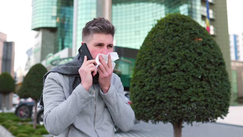 Young Man Navigates the Flu Season with Smartphone in Hand, Seeking Aid. In a poignant portrayal of a modern health crisis, the image conveys the young man's reliance on technology