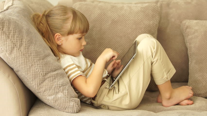 Little girl lying on sofa with tablet and smiling
