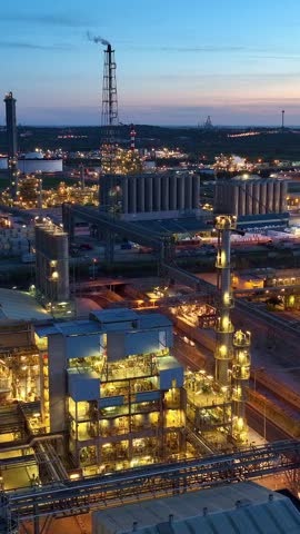 vertical video: oil refineries in and oil tanks at night, drone view of petrochemical plants, petroleum manufacturing, chemical plant in the evening. High quality FullHD footage