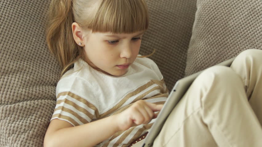 Little girl with tablet playing games and smiling

