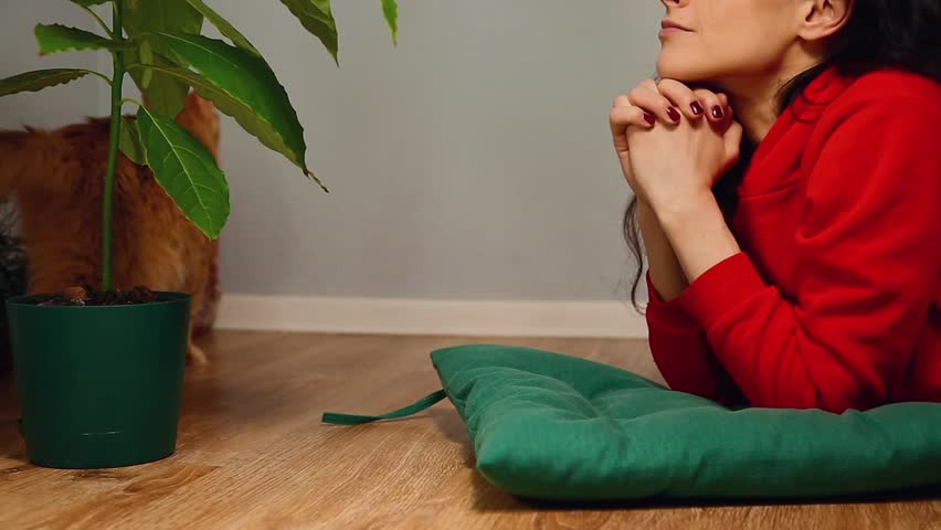 Young smiling thinking woman carefree lying on the floor and thinking, dreaming about holiday in red dress and looking on her orange playful cat