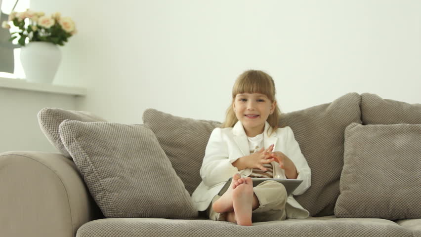 Little girl sitting on sofa with tablet and laughing
