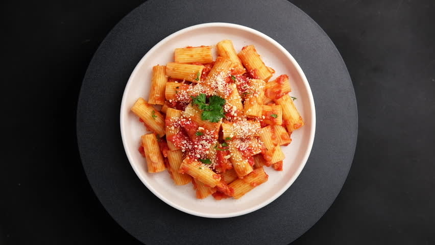 Rigatoni macaroni with fresh tomatoes sauce in white plate.topped with parmesan cheese and parsley.Top view.