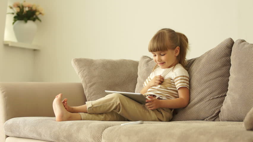 Girl with tablet sitting on sofa and laughing
