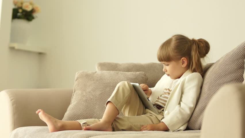 Little girl sitting on the couch with a tablet with ok hand sign
