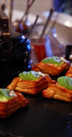 Flaky kiwi fruit pastries displayed on a dark buffet table with warm indoor lighting. Fresh breakfast dessert concept. Appetizing and inviting sweet treat.