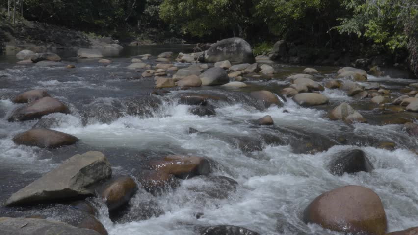 Slow-motion river water flowing over rocks, with a forest backdrop in a wide-angle shot.