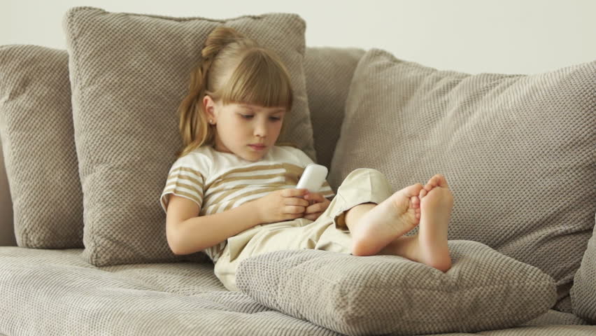 Little girl lying on the couch with the phone and smiling

