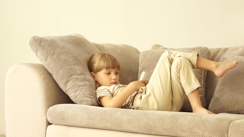Little girl lying on the sofa with phone and showing thumbs
