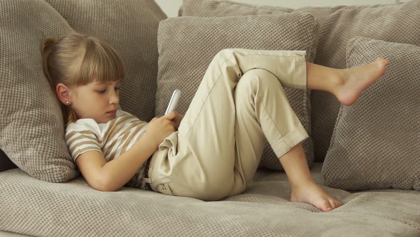 Little girl lying on the sofa and writing sms
