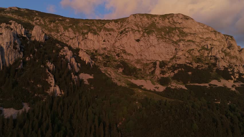 Cinematic sunset aerial footage of the western Bucegi Mountains ridge, the hiking trail leading to Batrana Refuge, Strungile Mari peaks, Saua Strunga, under warm golden hour light and glowing clouds