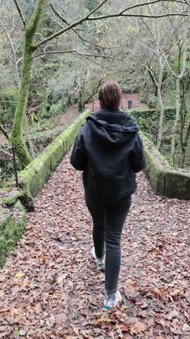 Woman walking along an old stonebridge covered in fallen autumn leaves