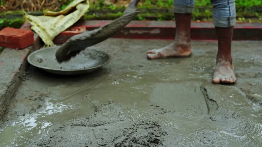A raw, real-life view of a remote rural Indian construction site where barefoot laborers mix and handle cement by shovel, highlighting hard work, resilience, and traditional building practices.