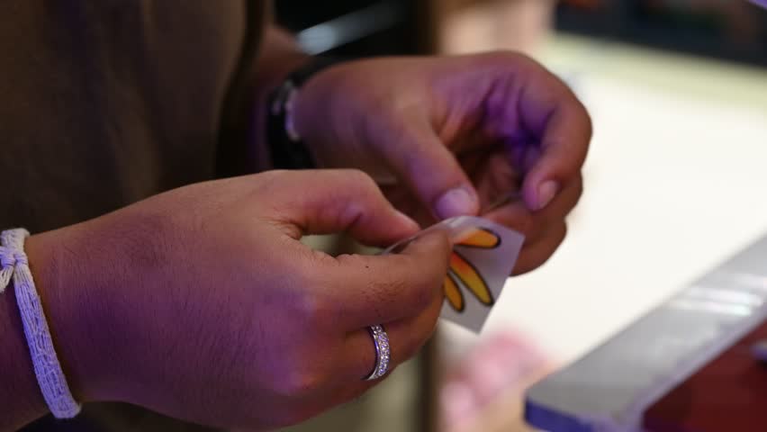 Bangkok, Thailand - 18th December 2025: Man manually printing alphabets on a pouch using an industrial printing machine, showcasing hands-on packaging, craftsmanship, manufacturing process, and small-scale production.