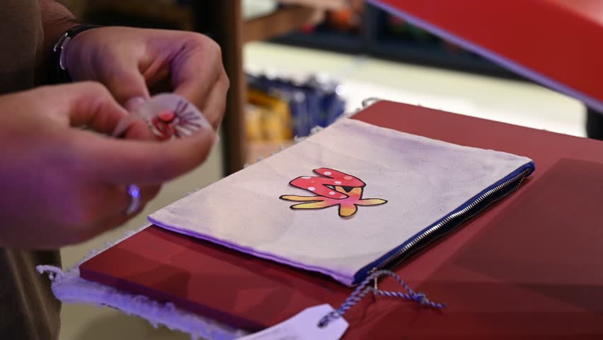 Bangkok, Thailand - 18th December 2025: Man manually printing alphabets on a pouch using an industrial printing machine, showcasing hands-on packaging, craftsmanship, manufacturing process, and small-scale production.