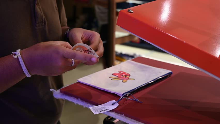 Bangkok, Thailand - 18th December 2025: Man manually printing alphabets on a pouch using an industrial printing machine, showcasing hands-on packaging, craftsmanship, manufacturing process, and small-scale production.